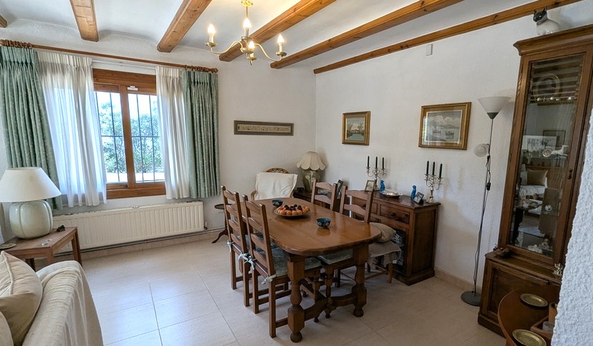 Salle à manger traditionnelle avec poutres en bois apparentes, table en bois massif et buffet classique. Comprend un radiateur et une fenêtre avec grilles de sécurité.