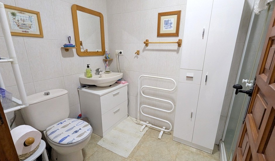 Salle de bain fonctionnelle avec meuble vasque blanc, miroir à cadre en bois et colonnes de rangement. Équipée d'un sèche-serviettes et de murs carrelés.