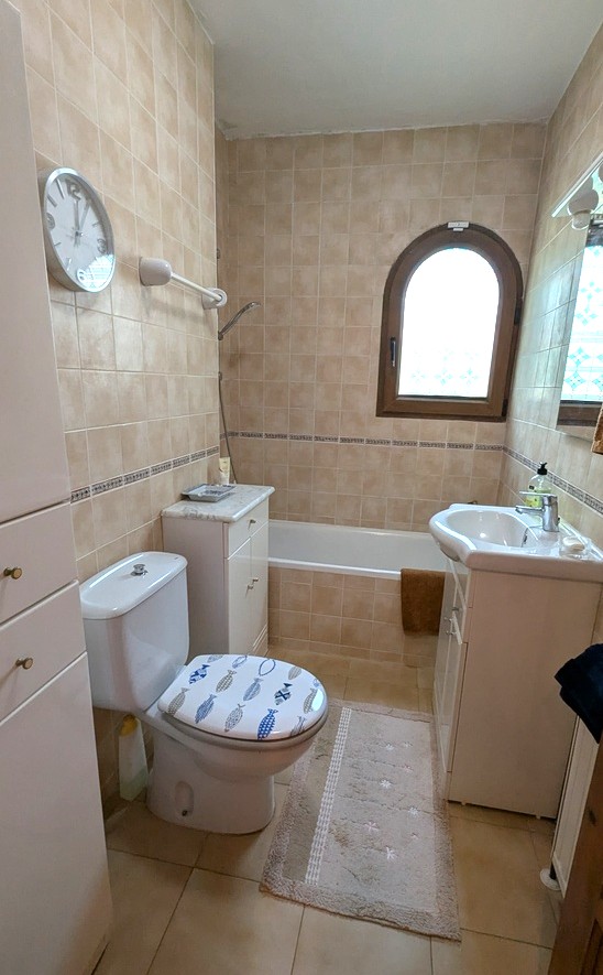 Salle de bain traditionnelle avec carrelage beige, baignoire intégrée et fenêtre cintrée en bois. Comprend un meuble vasque blanc et des colonnes de rangement.