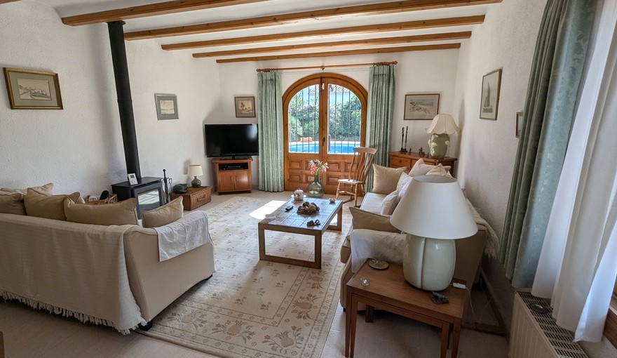 Salon avec poutres en bois apparentes, poêle à bois et portes voûtées en bois ouvrant sur la piscine. Décoration traditionnelle aux tons neutres et atmosphère chaleureuse.
