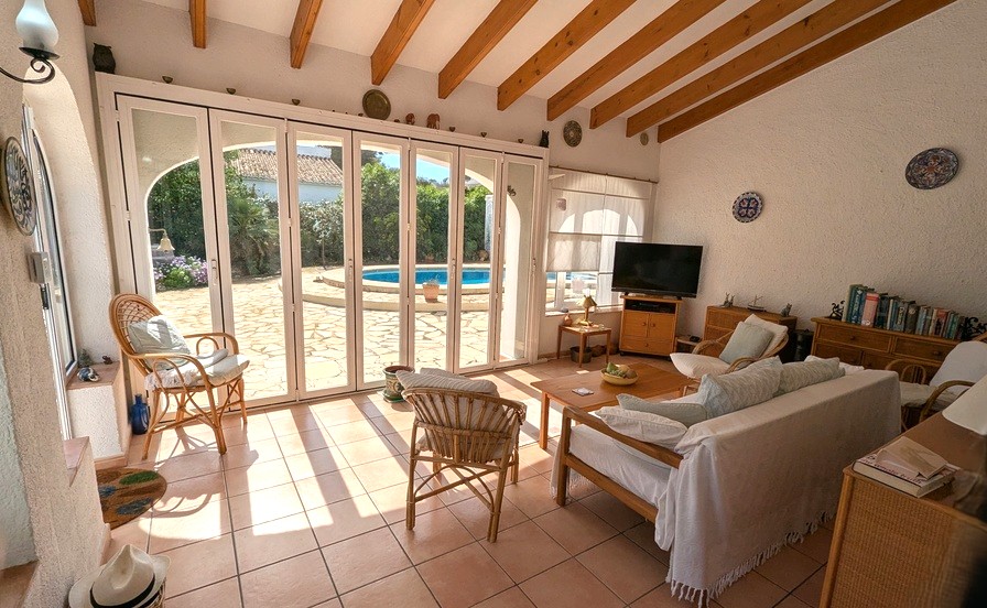 Salon lumineux avec poutres en bois apparentes, sol en terre cuite et grandes baies vitrées pliantes ouvrant sur la terrasse de la piscine.