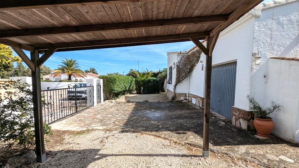 Vue depuis l'abri de voiture en bois révélant l'allée pavée, le garage attenant et le portail en fer forgé menant à la rue.