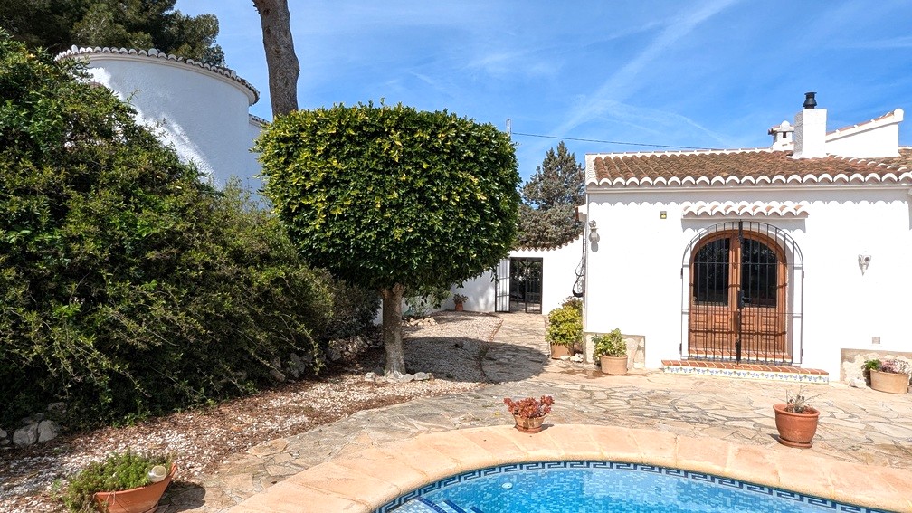 Vue extérieure de la villa avec piscine en mosaïque, terrasse en pierre et façade blanche traditionnelle dotée de portes en bois voûtées et de ferronnerie noire.
