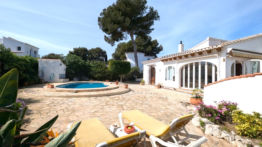 Vue extérieure de la villa méditerranéenne avec piscine, terrasse en pierre naturelle et façade blanche aux poutres en bois et grandes baies vitrées voûtées.