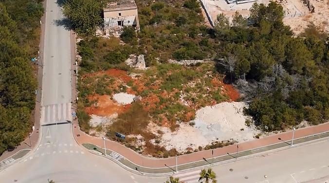 Vue aérienne de la parcelle d'angle de 1 000 m² à Villas del Vent, montrant le terrain avec terre rouge, pins environnants et infrastructures routières.