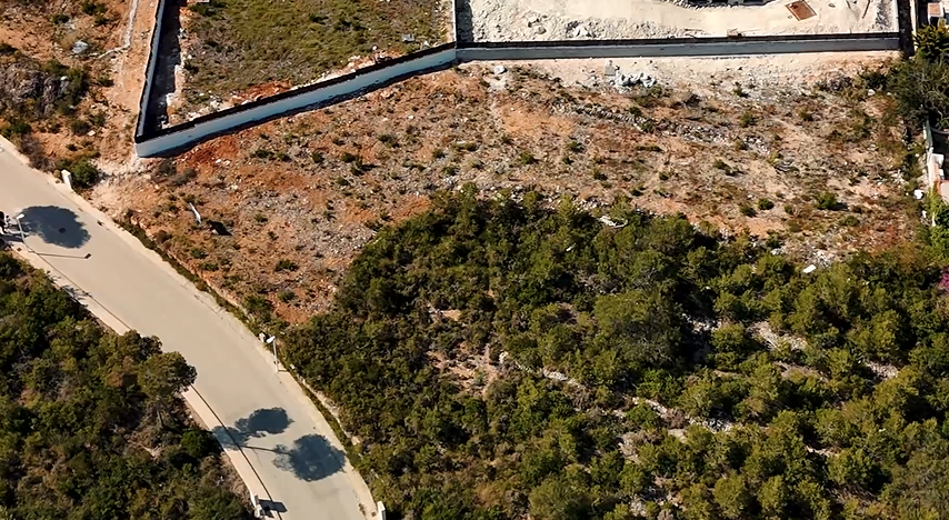 Vue aérienne du terrain de 1 528 m² à Lomas del Rey, illustrant la zone excavée, le mur de soutènement et l'accès direct par la route résidentielle asphaltée.