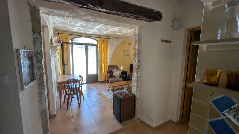 Arche traditionnelle en pierre de Tosca avec poutre en bois, ouvrant sur un espace de vie avec carrelage en terre cuite et porte vitrée cintrée.
