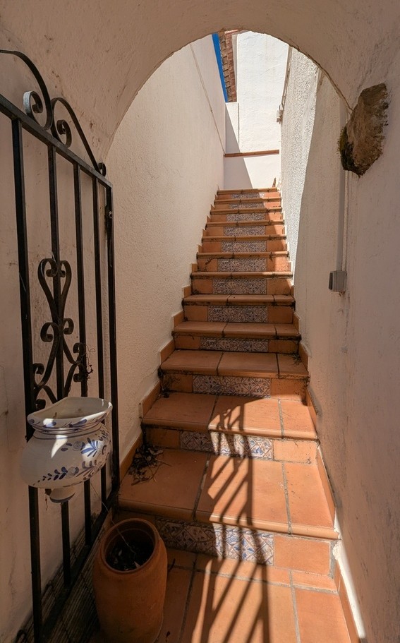Escalier extérieur en terre cuite avec contremarches en céramique décorée, accessible par une arche blanche et une grille en fer forgé.