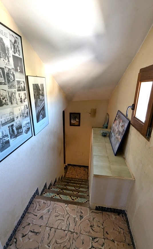 Escalier intérieur doté de carrelages traditionnels et de contremarches en mosaïque. Une fenêtre en bois et des cadres décoratifs complètent cet espace authentique.