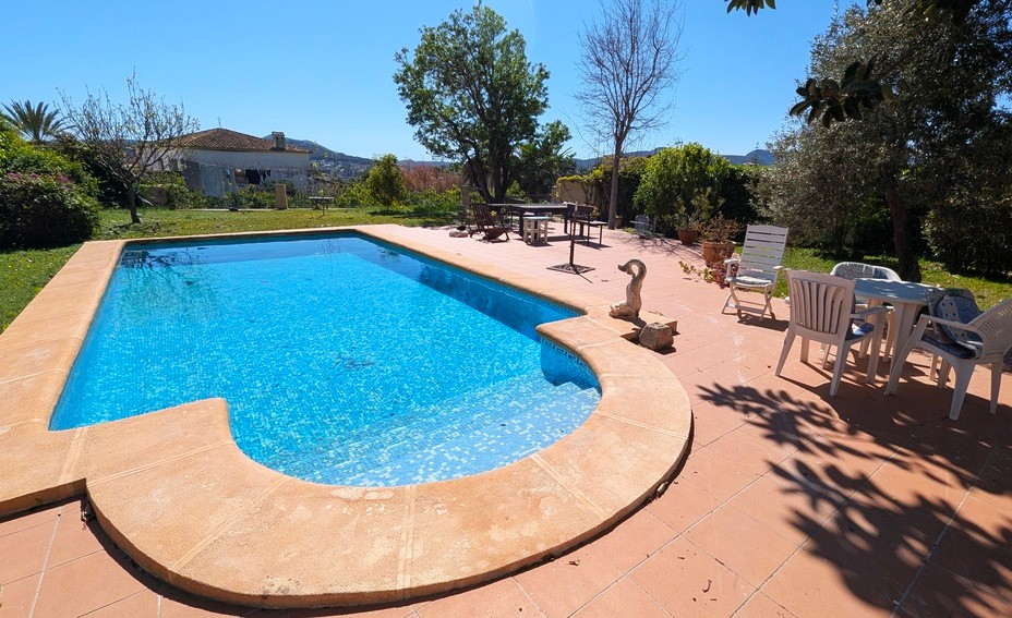 Piscine privée avec mosaïque bleue, entourée d'une vaste terrasse en terre cuite et d'un jardin méditerranéen offrant une vue dégagée sur les collines.