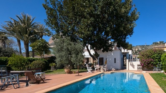 Piscine privée rectangulaire avec terrasse en terre cuite, entourée d'un jardin méditerranéen arboré offrant une vue dégagée sur la montagne Montgó.
