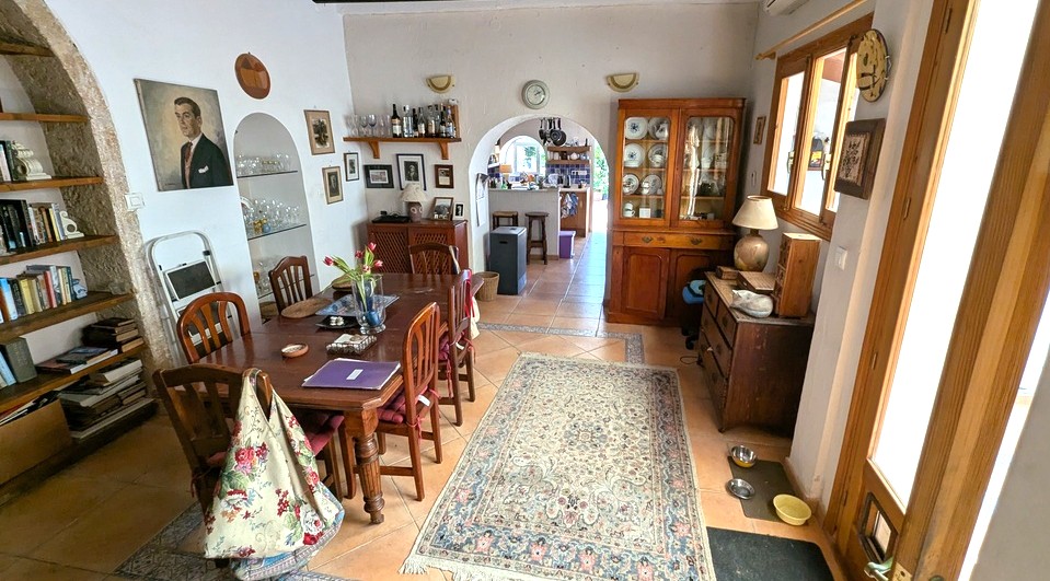 Salle à manger spacieuse avec sol en terre cuite, table en bois et arches en pierre Tosca authentique intégrant des étagères, s'ouvrant sur la cuisine.