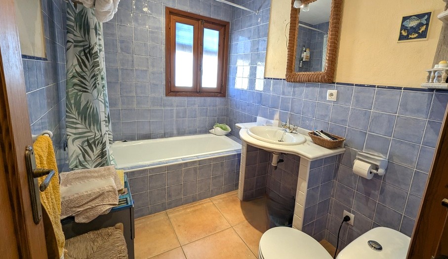 Salle de bain traditionnelle avec carrelage bleu, baignoire encastrée et vasque sur plan en marbre. Elle dispose d'un sol en terre cuite et d'une fenêtre en bois.