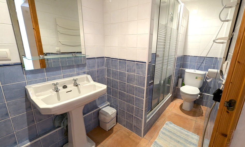 Salle de bain traditionnelle avec carrelage mural bleu et blanc, lavabo sur colonne, sol en terre cuite et douche avec paroi vitrée.