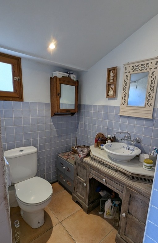 Salle de bains avec meuble vasque en bois rustique, plan de travail en marbre, vasque fleurie et carrelage mural bleu clair complété par un sol en terre cuite.