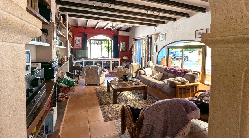 Salon spacieux avec poutres apparentes en bois sombre, arches en pierre Tosca, sol en terre cuite et grandes fenêtres apportant une lumière naturelle.