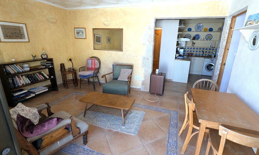 Séjour de l'appartement d'invités avec sol en terre cuite, murs texturés ocres et une arche en pierre de Tosca ouvrant sur la kitchenette équipée.