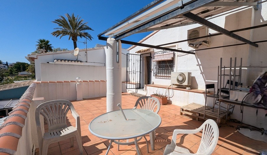 Terrasse orientée sud au premier étage avec carrelage en terre cuite, structure de pergola métallique et unités de climatisation, offrant une vue sur les palmiers.