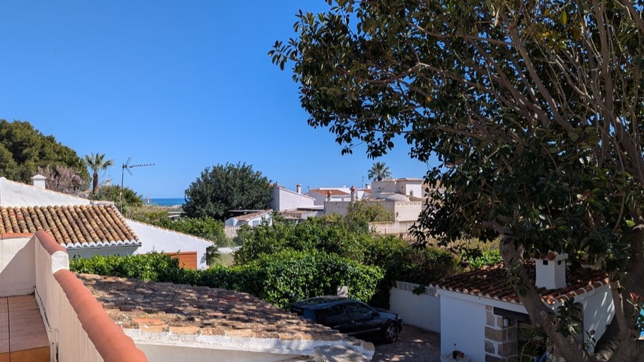 Vue depuis la terrasse supérieure surplombant les toits de tuiles traditionnels, la végétation dense et l'horizon marin au loin.