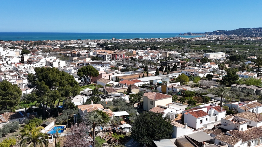 Vue panoramique depuis la terrasse sur les toits de Javea Pueblo, s'étendant vers la mer Méditerranée et le littoral lointain sous un ciel clair.