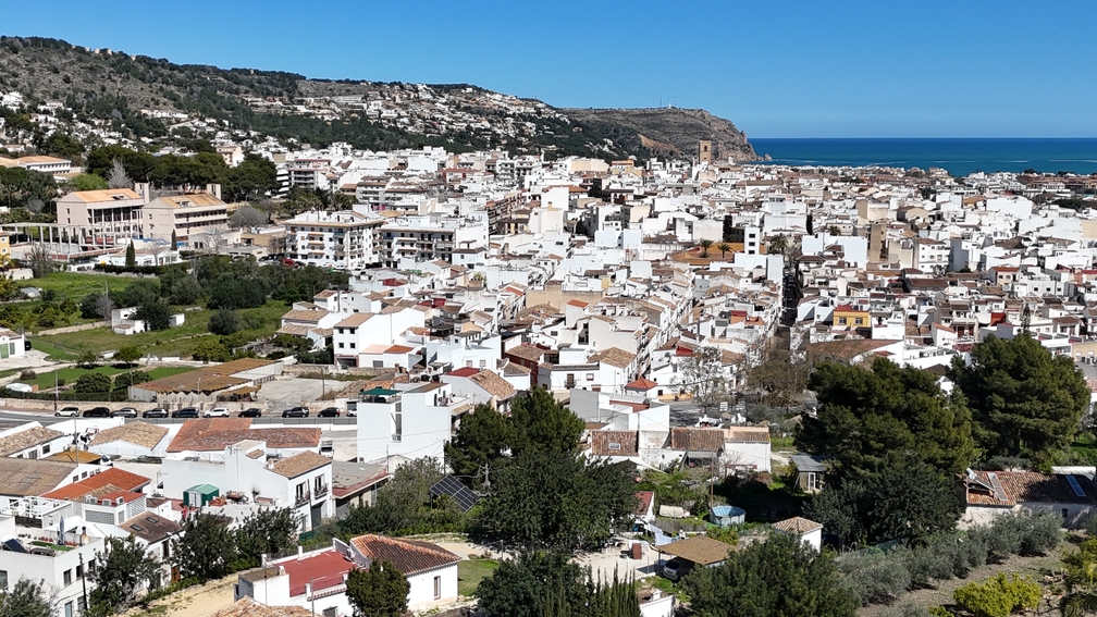 Vue panoramique sur le centre historique de Javea, illustrant l'architecture blanche typique, le clocher de l'église et la mer Méditerranée en arrière-plan.