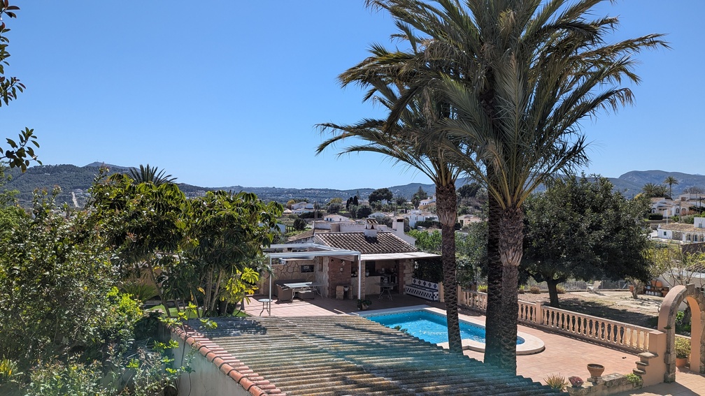 Vue surélevée de la piscine privée et de la terrasse, incluant une cuisine d'été traditionnelle, des palmiers et un panorama sur la campagne de Javea.