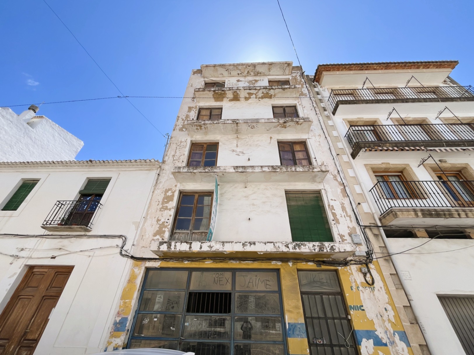 Façade de quatre étages avec un local commercial au rez-de-chaussée. Le bâtiment présente des balcons filants et des menuiseries en bois, offrant un fort potentiel de rénovation.