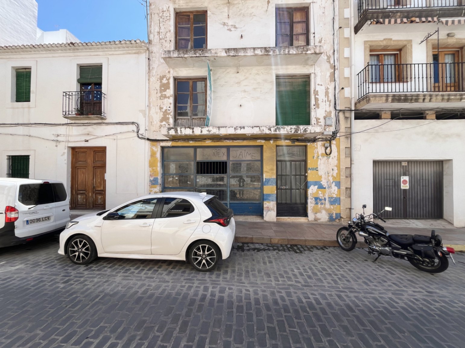 Façade extérieure du bâtiment à Jávea comprenant un local commercial au rez-de-chaussée, des balcons aux étages et des fenêtres en bois sur une rue pavée.