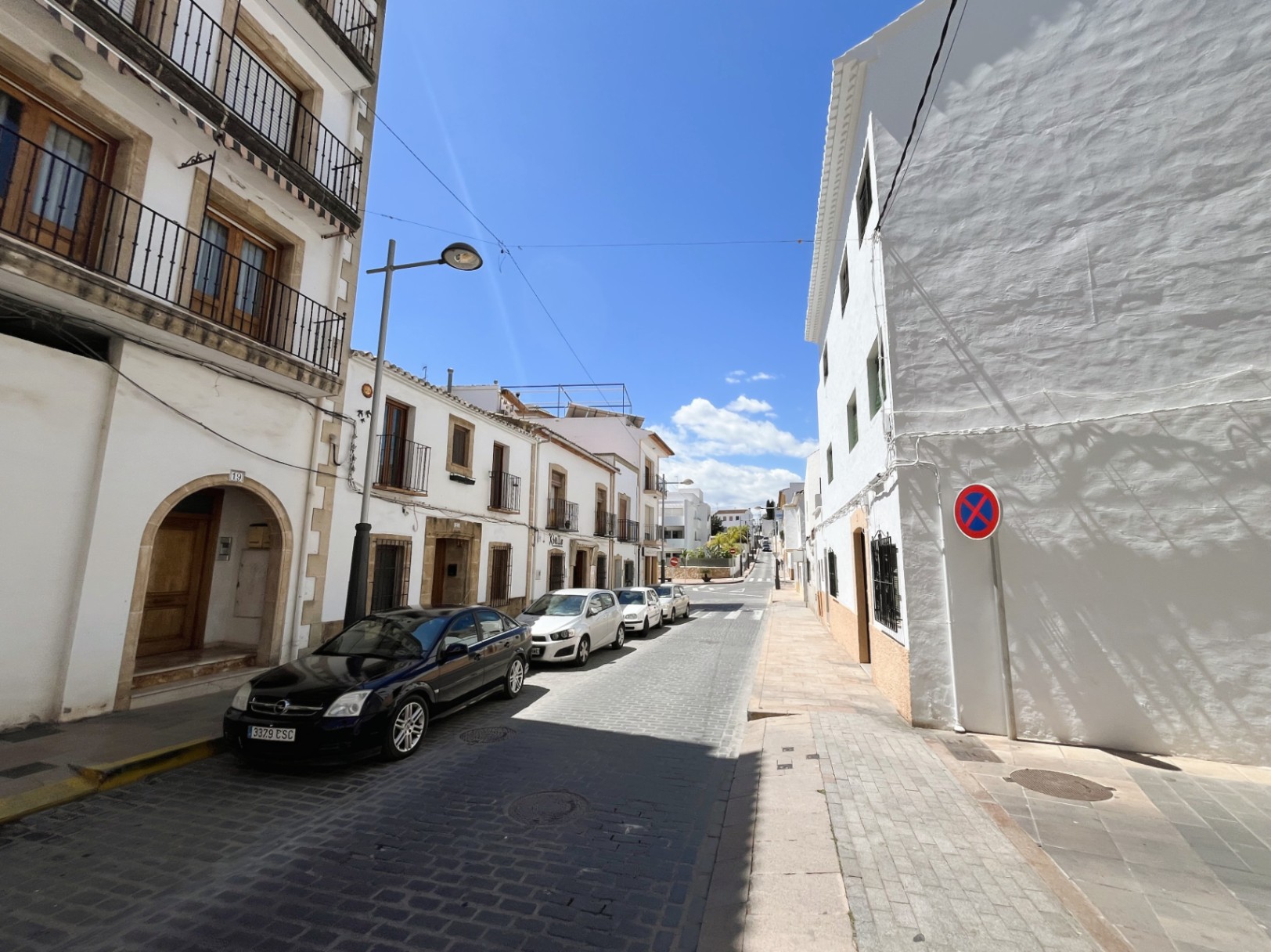 Façade extérieure du bâtiment située dans une rue pavée de la vieille ville de Jávea, avec des arches en pierre Tosca et des balcons traditionnels en fer forgé.