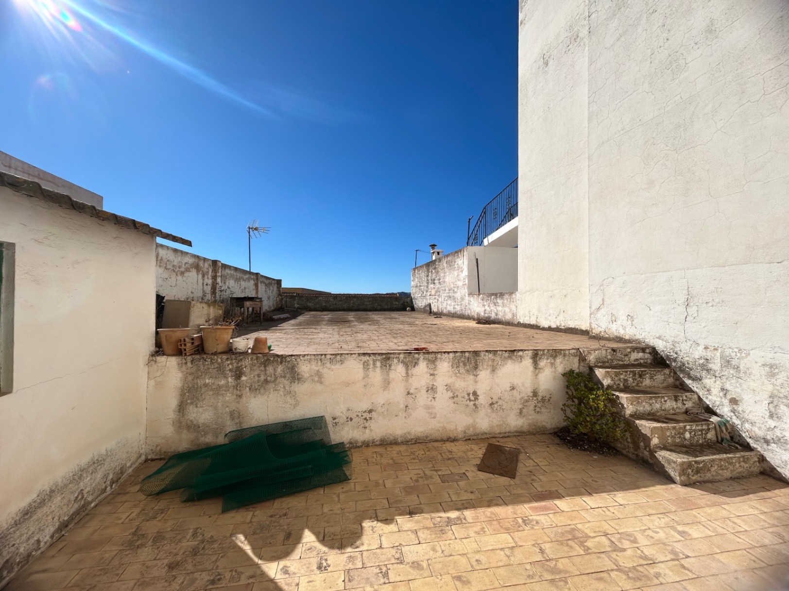 Terrasse sur le toit à deux niveaux avec revêtement en carrelage, escalier en pierre et murs blancs, offrant un espace extérieur à fort potentiel.