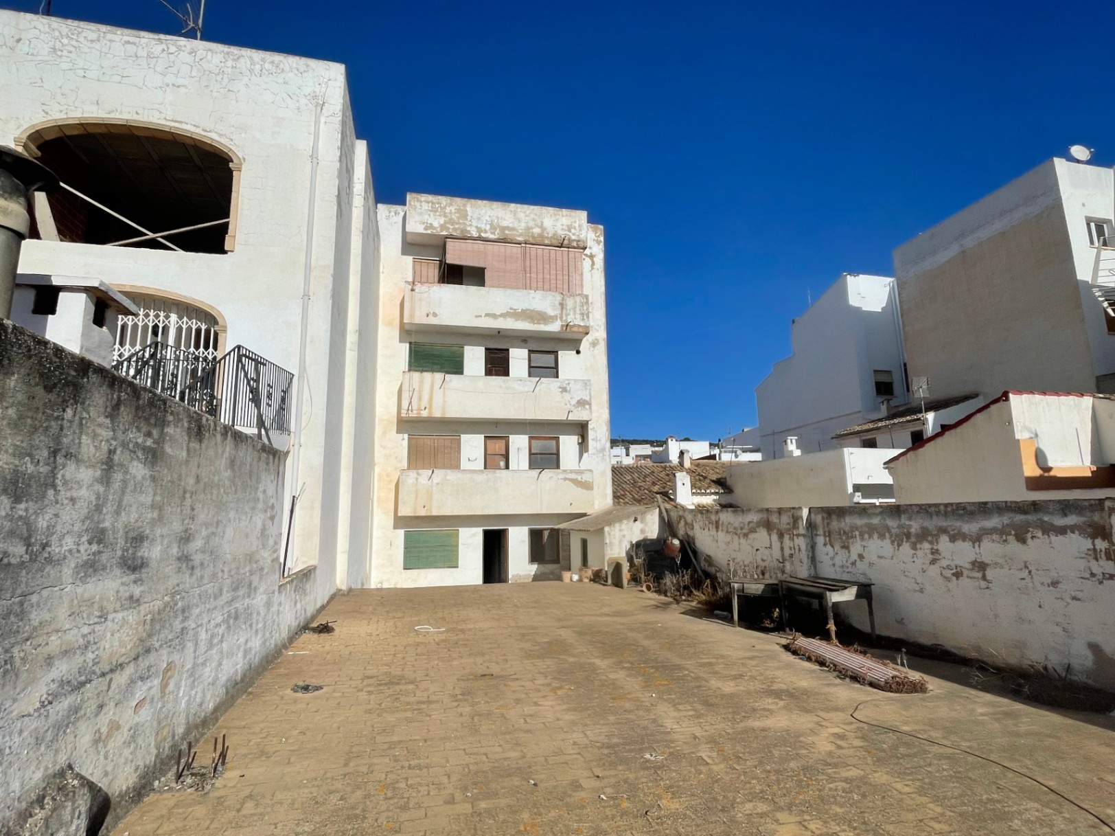 Vue arrière du bâtiment de quatre étages avec une grande cour pavée et des murs d'enceinte. La façade présente des balcons et des fenêtres d'origine sous un ciel dégagé.