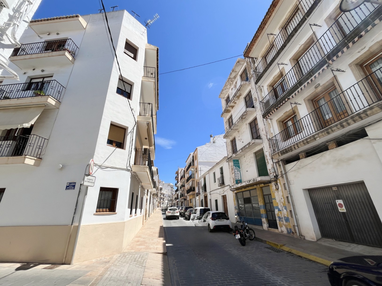 Vue extérieure de l'immeuble de quatre étages au centre de Jávea, présentant une façade blanche avec balcons en fer forgé et un grand local commercial au rez-de-chaussée.
