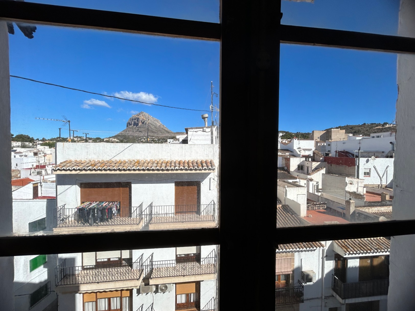 Vue urbaine depuis l'intérieur à travers un cadre de fenêtre, donnant sur les toits de la vieille ville de Jávea et le sommet de la montagne Montgó.