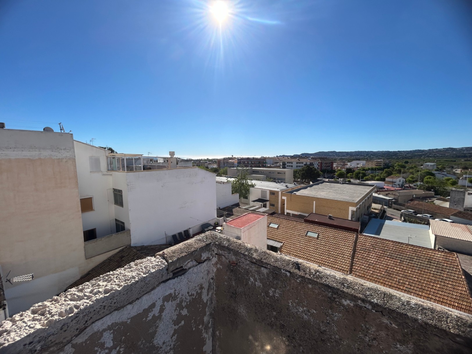 Vues panoramiques depuis le toit-terrasse sur le centre de Jávea et la mer Méditerranée, montrant les toits de tuiles traditionnels et les reliefs montagneux au loin.