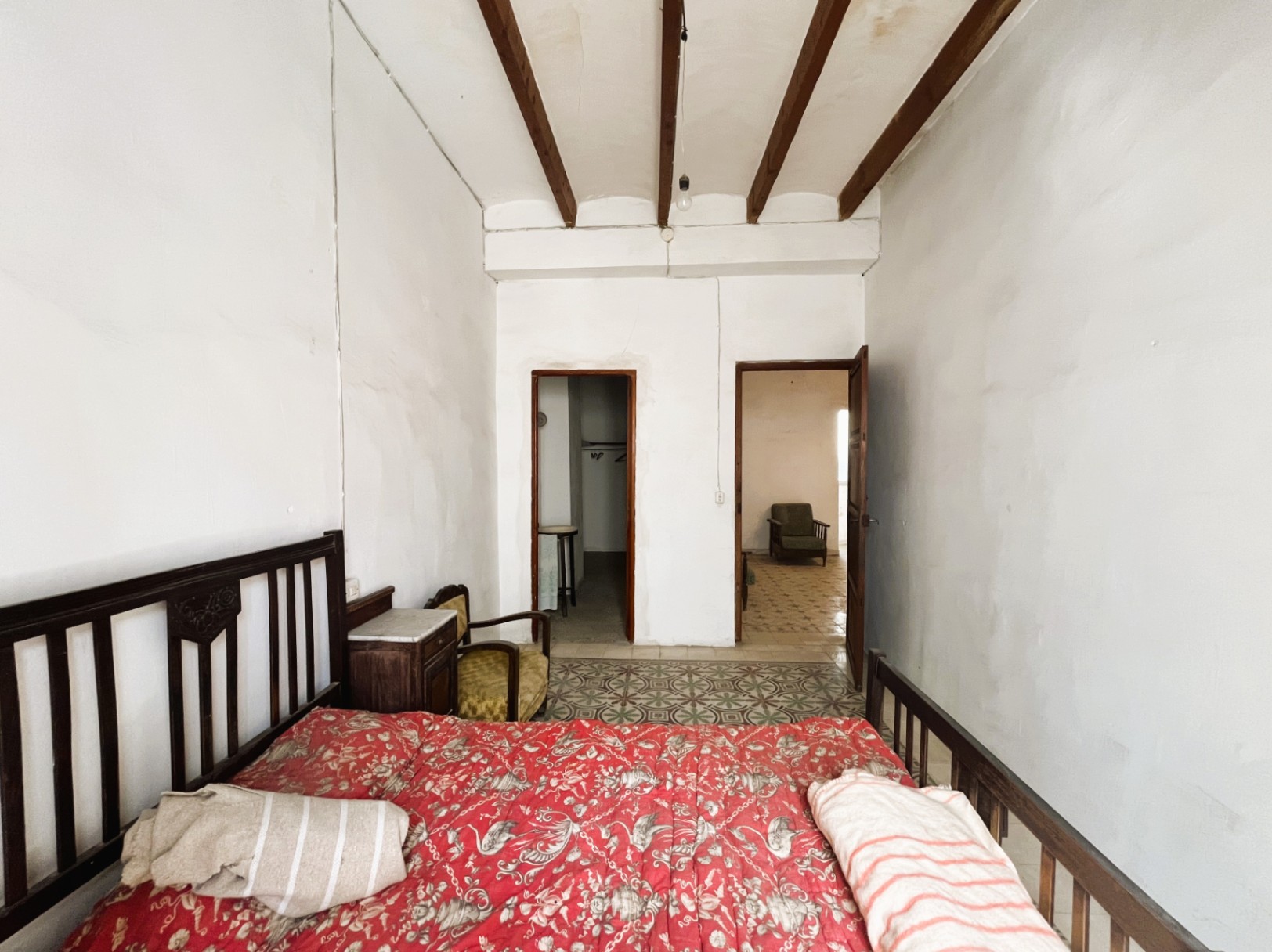 Chambre avec hauts plafonds et poutres en bois apparentes, sols en carreaux de ciment d'origine et mobilier d'époque ouvrant sur des pièces attenantes.