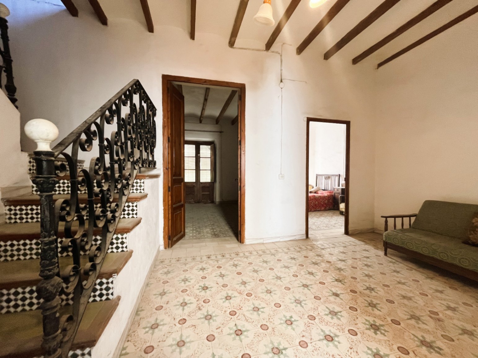 Hall de distribution avec carrelage hydraulique d'époque, poutres en bois apparentes et un escalier de caractère avec rampe en fer forgé.