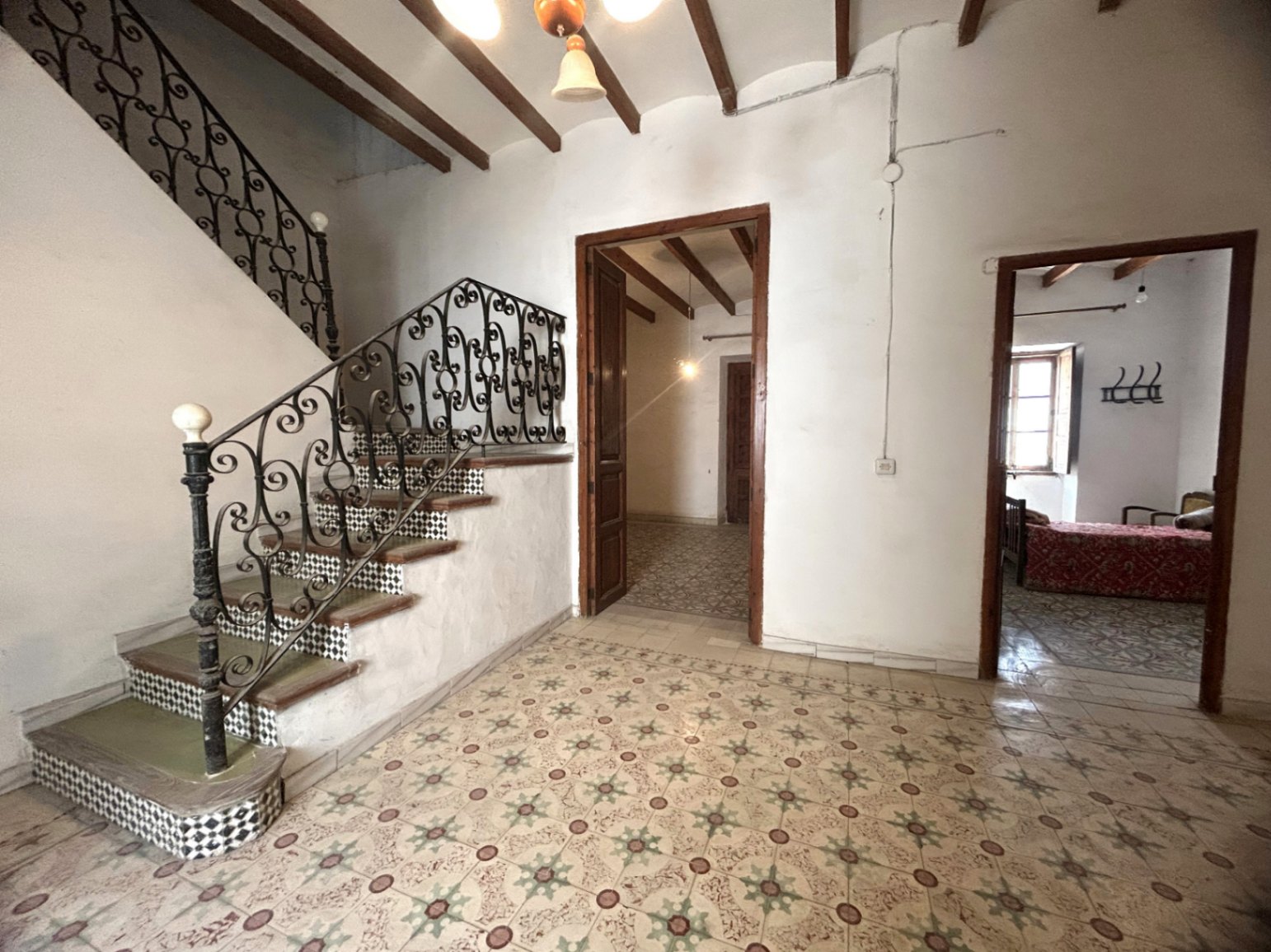 Hall d'entrée principal avec sols en mosaïque d'époque, poutres en bois apparentes et un escalier de caractère avec rampe en fer forgé et contremarches carrelées.