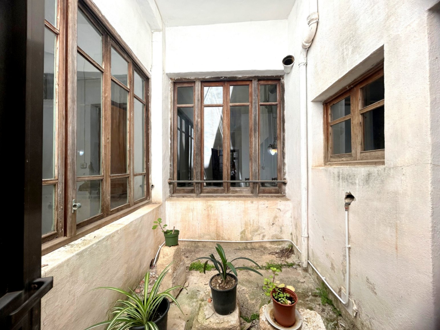 Puits de lumière central avec de grandes fenêtres en bois d'origine et des murs blancs, offrant éclairage naturel et ventilation au cœur de la demeure historique.