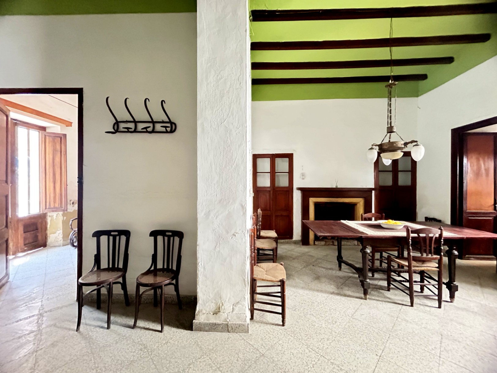 Salle à manger traditionnelle avec poutres en bois d'origine, hauts plafonds verts et cheminée classique. Le mobilier d'époque et la lumière naturelle soulignent l'espace.