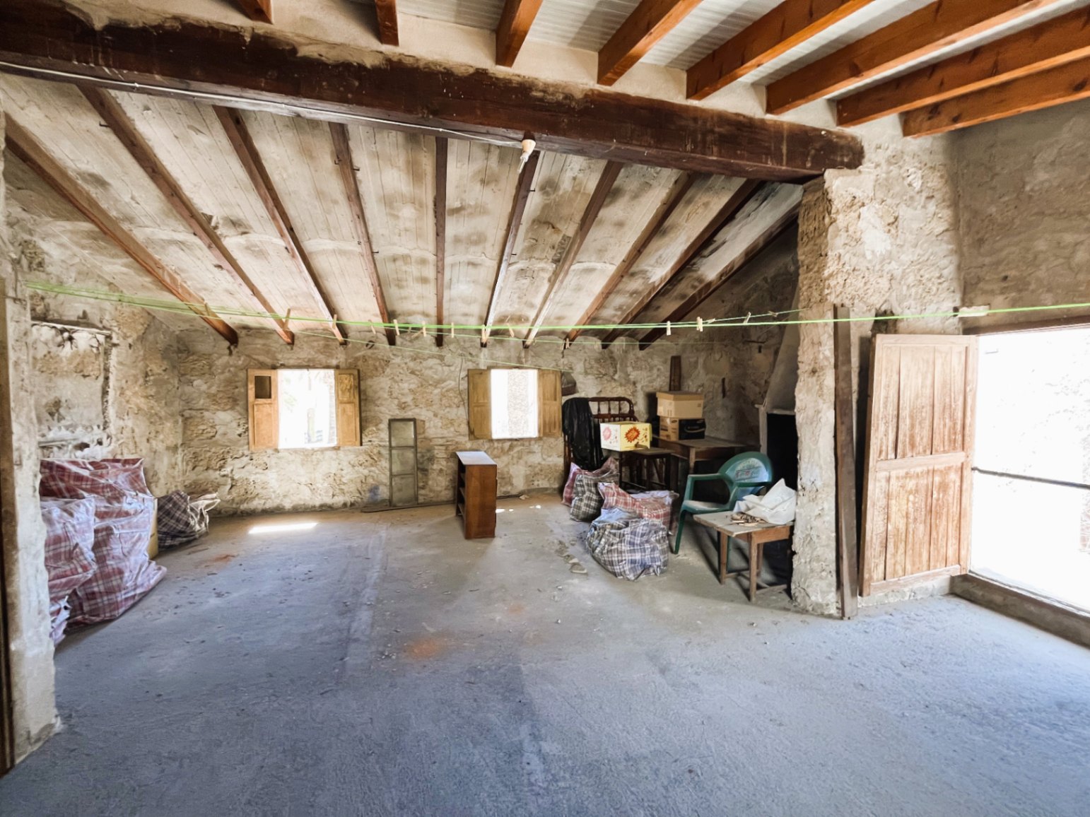 Combles spacieux avec poutres en bois et murs en pierre naturelle, caractérisés par une structure de toit inclinée et un fort potentiel de rénovation complète.