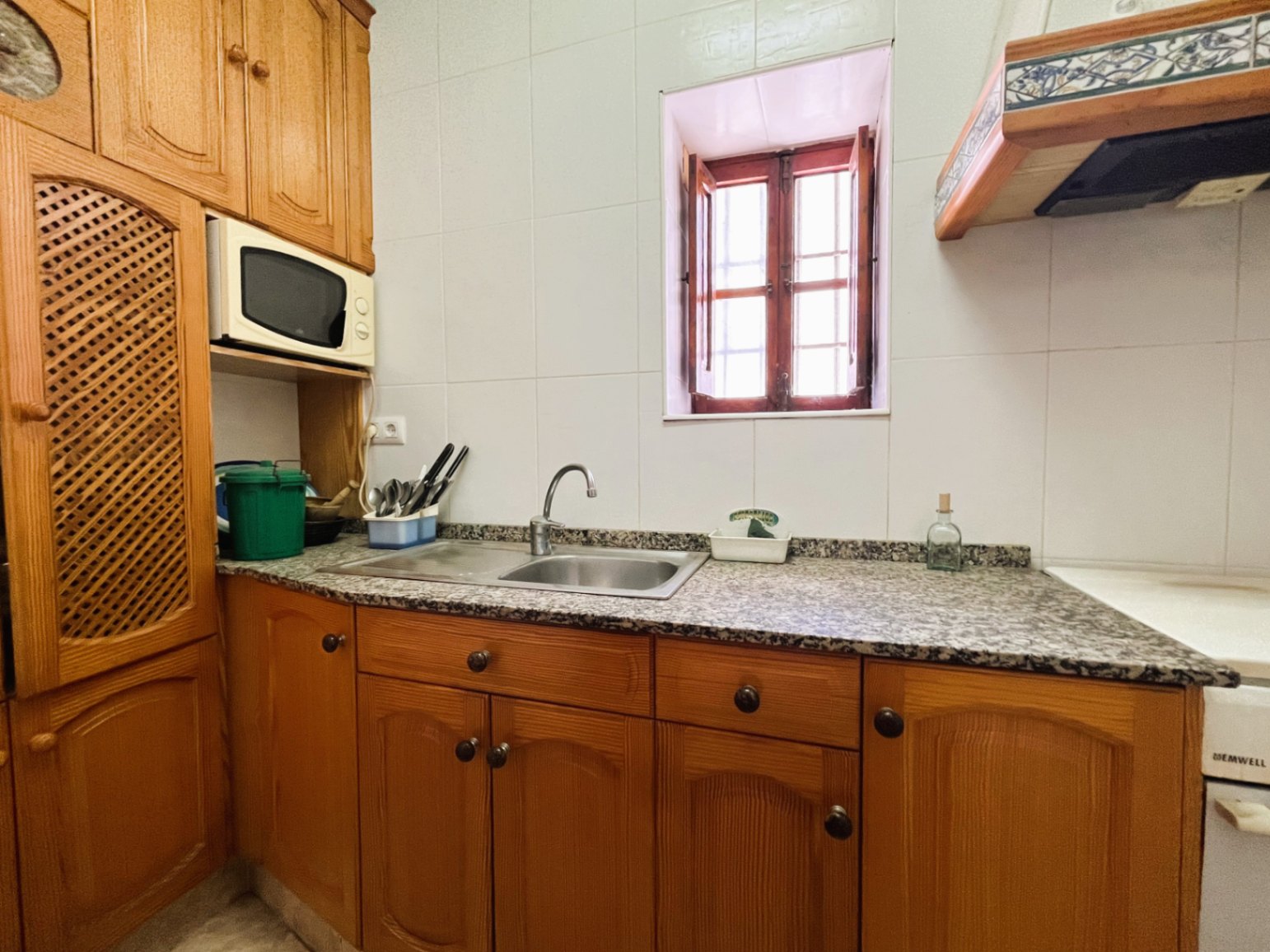 Cuisine fermée avec des meubles en bois traditionnel, un plan de travail en granit et une fenêtre à battants en bois apportant une lumière naturelle.