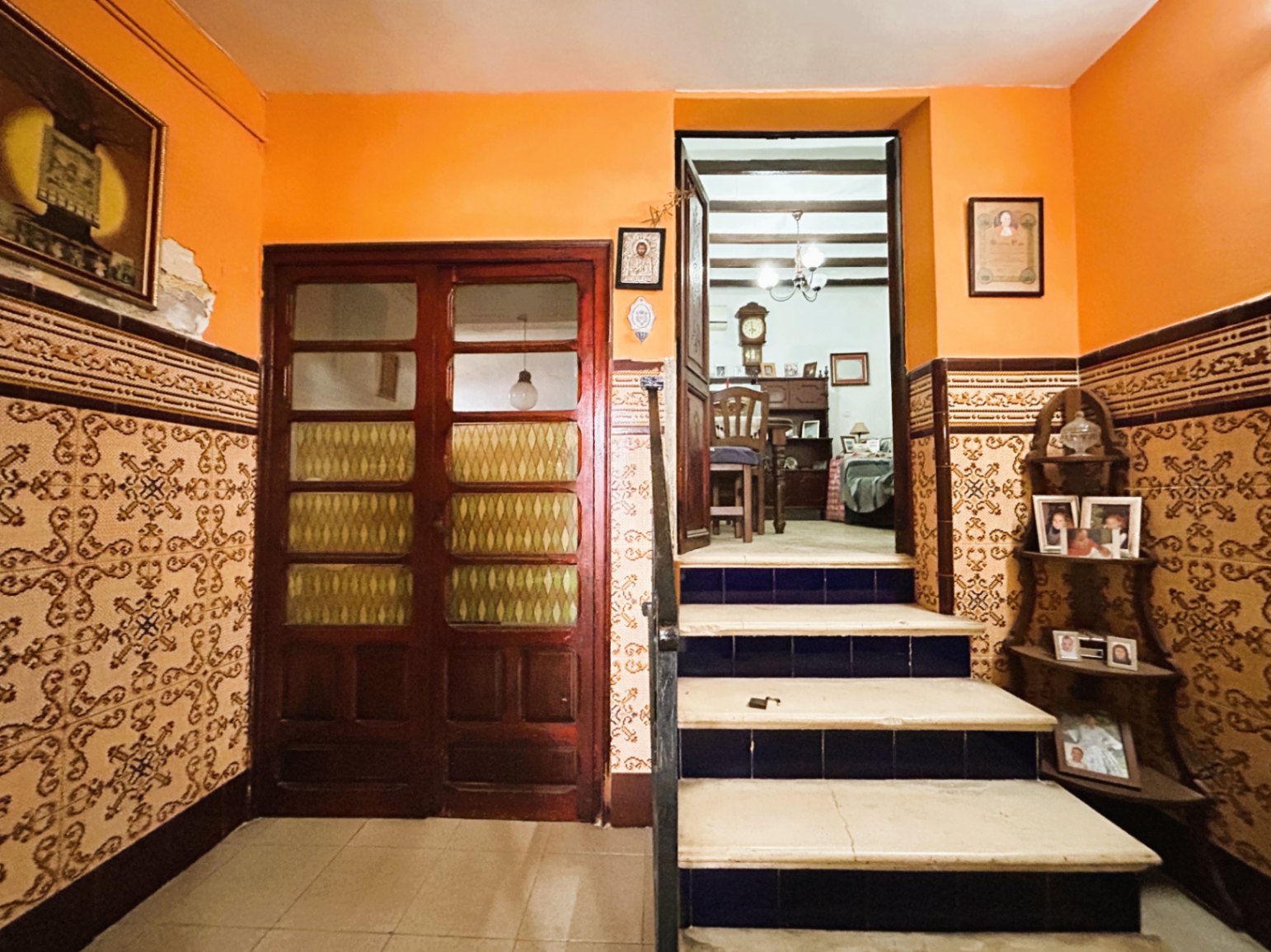 Entrée traditionnelle avec soubassement en azulejos, murs ocre et escalier en marbre aux contremarches bleues menant vers un espace de vie aux poutres apparentes.