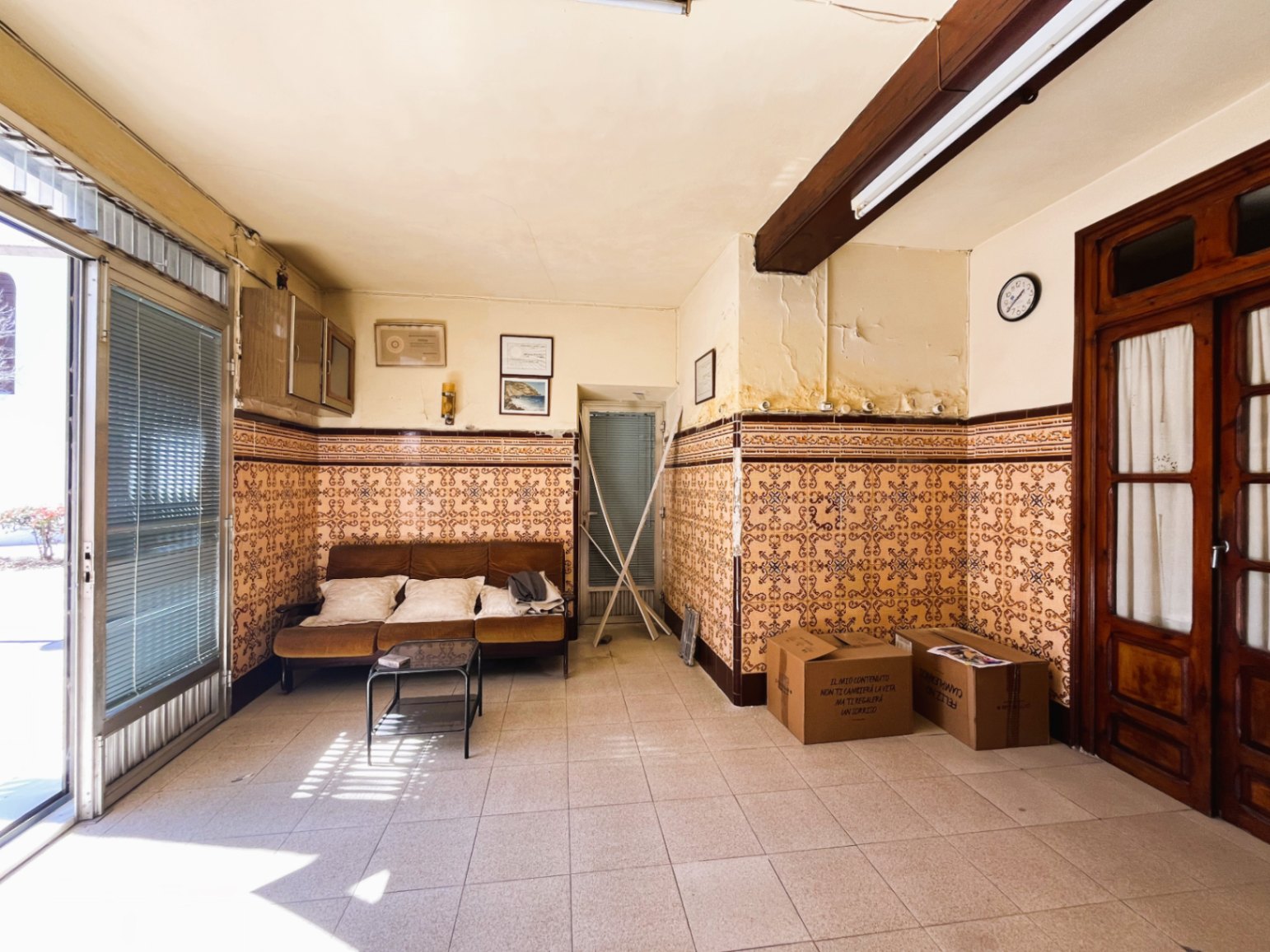 Espace de vie d'entrée avec des carreaux de faïence traditionnels, une poutre en bois apparente et une grande porte vitrée laissant entrer la lumière.