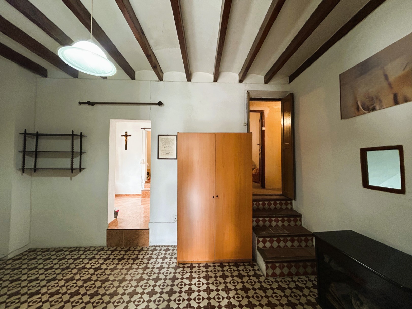 Espace intérieur avec poutres en bois apparentes, sol en carreaux de ciment d'origine et escaliers décoratifs menant aux niveaux supérieurs.