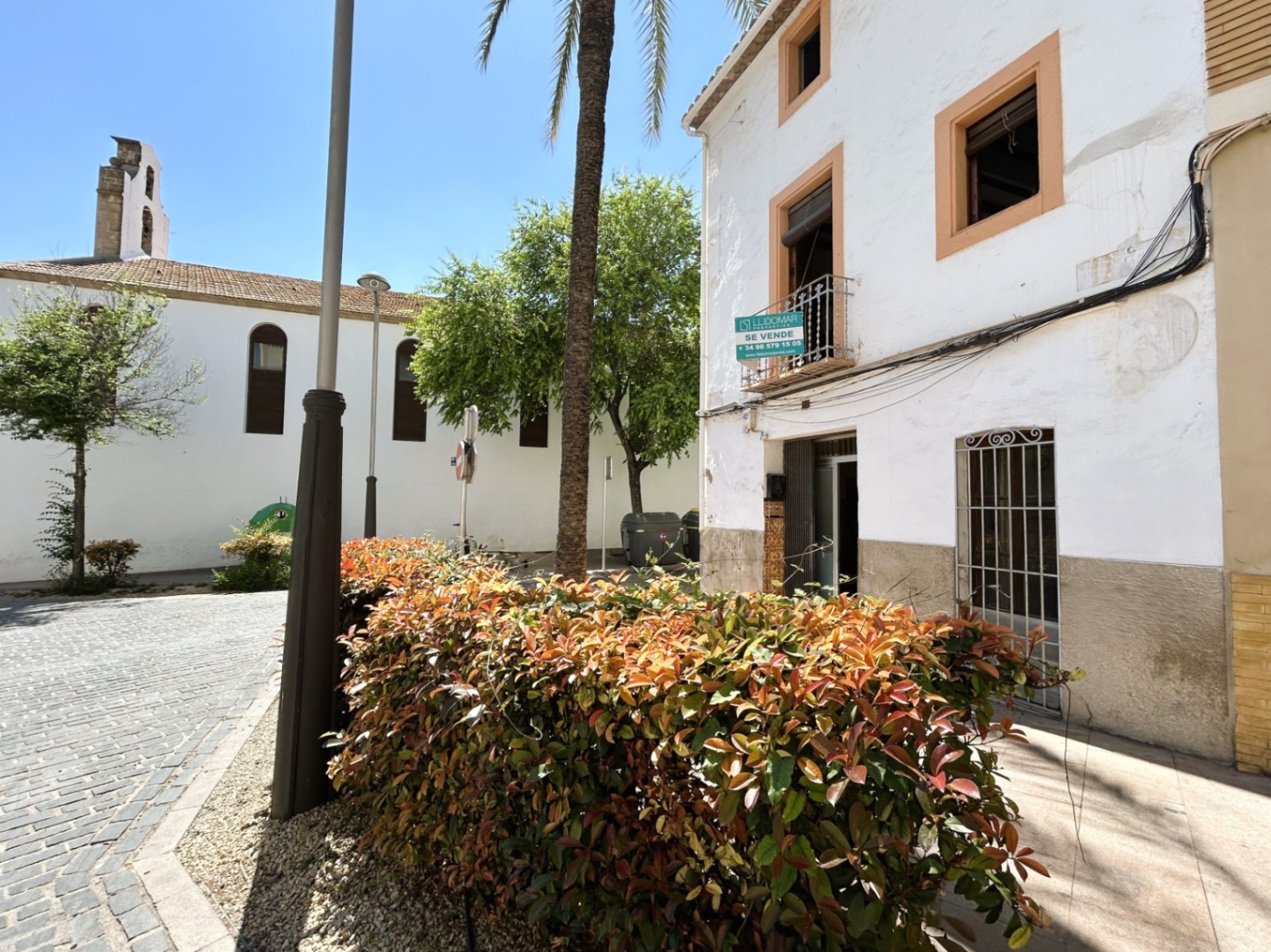 Façade traditionnelle blanche avec encadrements ocre, située sur une place pavée à côté d'une église historique dans la vieille ville de Jávea.