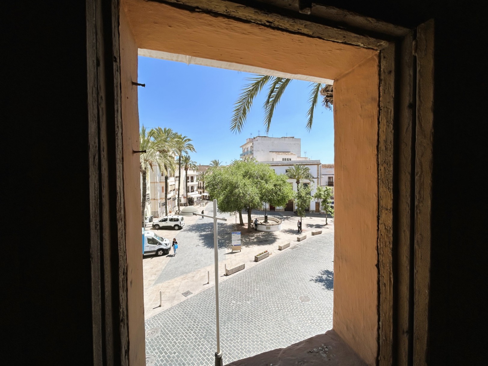 Vue depuis l'intérieur sur une place pavée du centre historique, soulignant l'épaisseur des murs traditionnels et la luminosité des palmiers environnants.