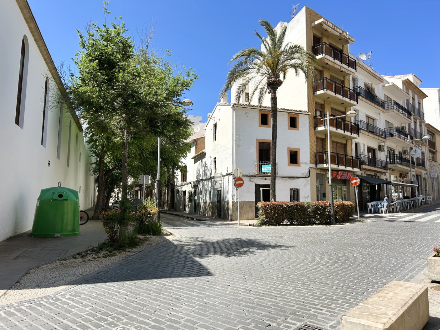 Vue extérieure de la façade blanche en angle située dans une rue pavée du centre historique de Jávea, agrémentée d'un palmier et d'un ciel dégagé.