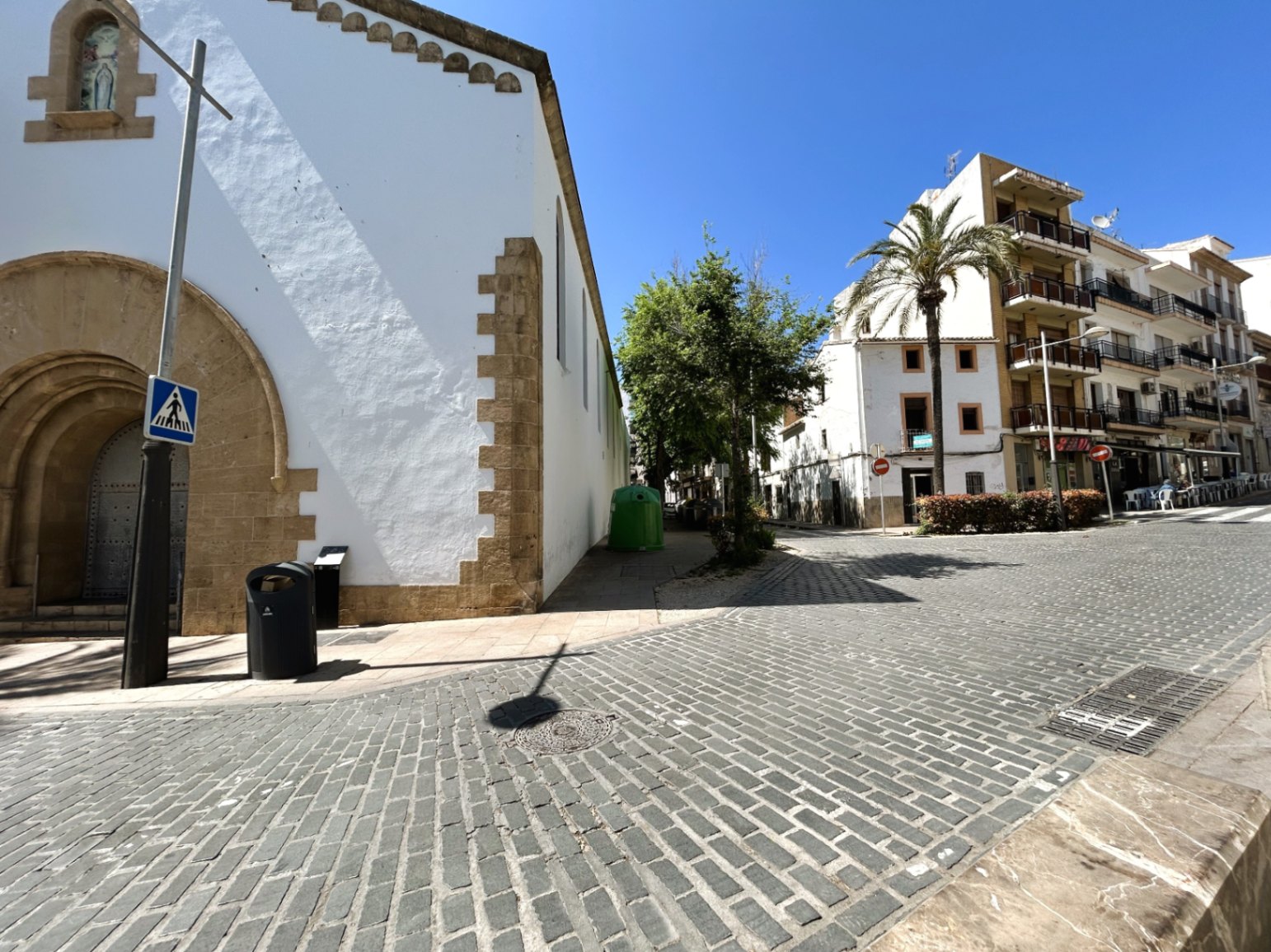 Vue extérieure de la rue pavée jouxtant un bâtiment historique aux arches en pierre de Tosca, au cœur du vieux quartier de Jávea.