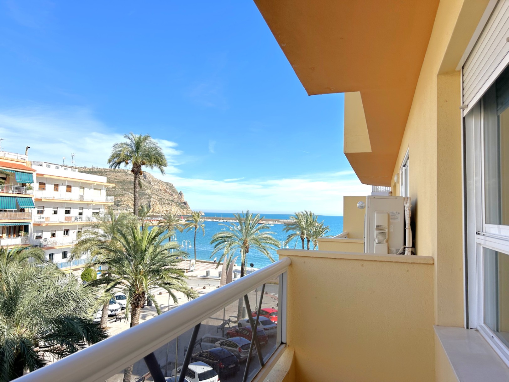 Balcon avec vue directe sur la mer et le port de Jávea, mettant en valeur les palmiers environnants et les menuiseries extérieures en aluminium.