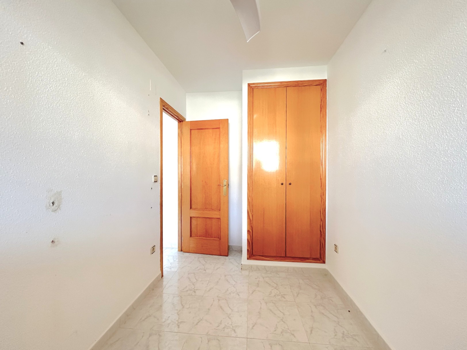 Couloir de distribution avec sol en grès cérame effet marbre, murs blancs et placard encastré en bois naturel intégré.